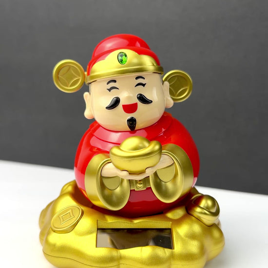 Solar powered rocking Chinese God of Wealth Cai Shen figurine in red and gold holding a gold ingot while sitting on a golden cloud base.