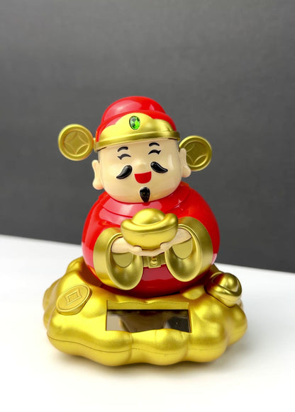 Solar powered rocking Chinese God of Wealth Cai Shen figurine in red and gold holding a gold ingot while sitting on a golden cloud base.
